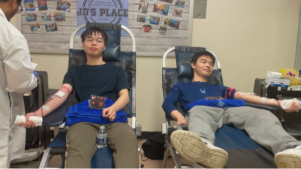 Two students in the middle of the blood donation procedure. They both have needles in their arms actively drawing blood.